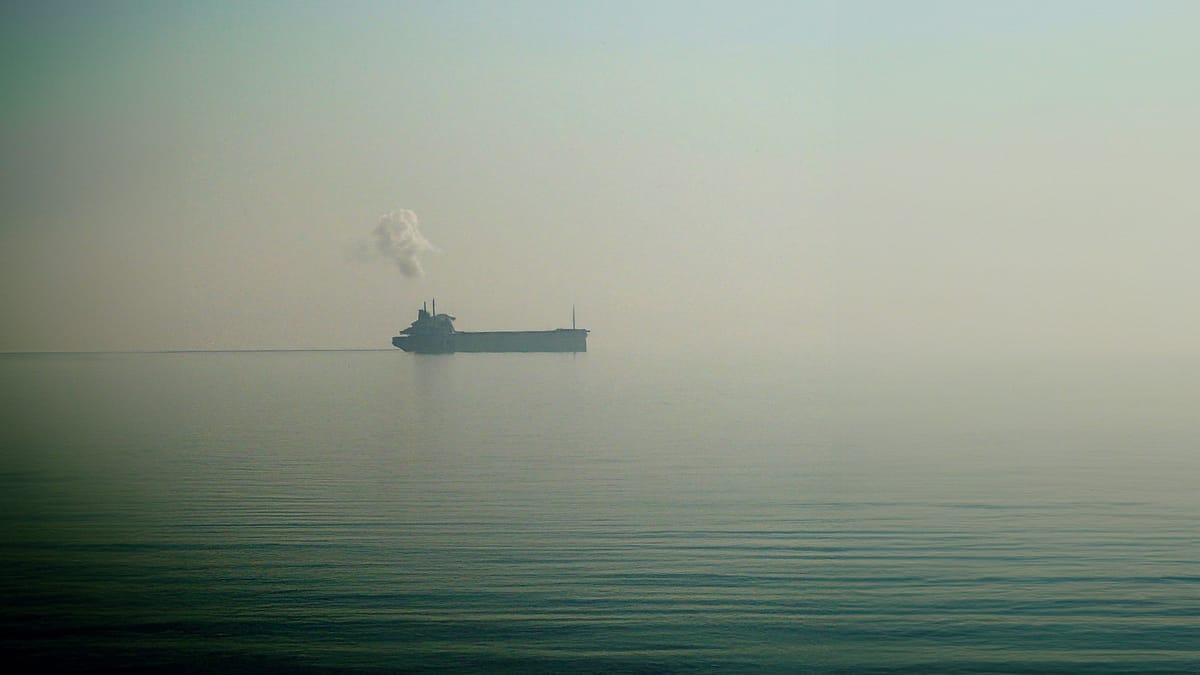 A cargo ship in the distance during the faint break of a foggy day