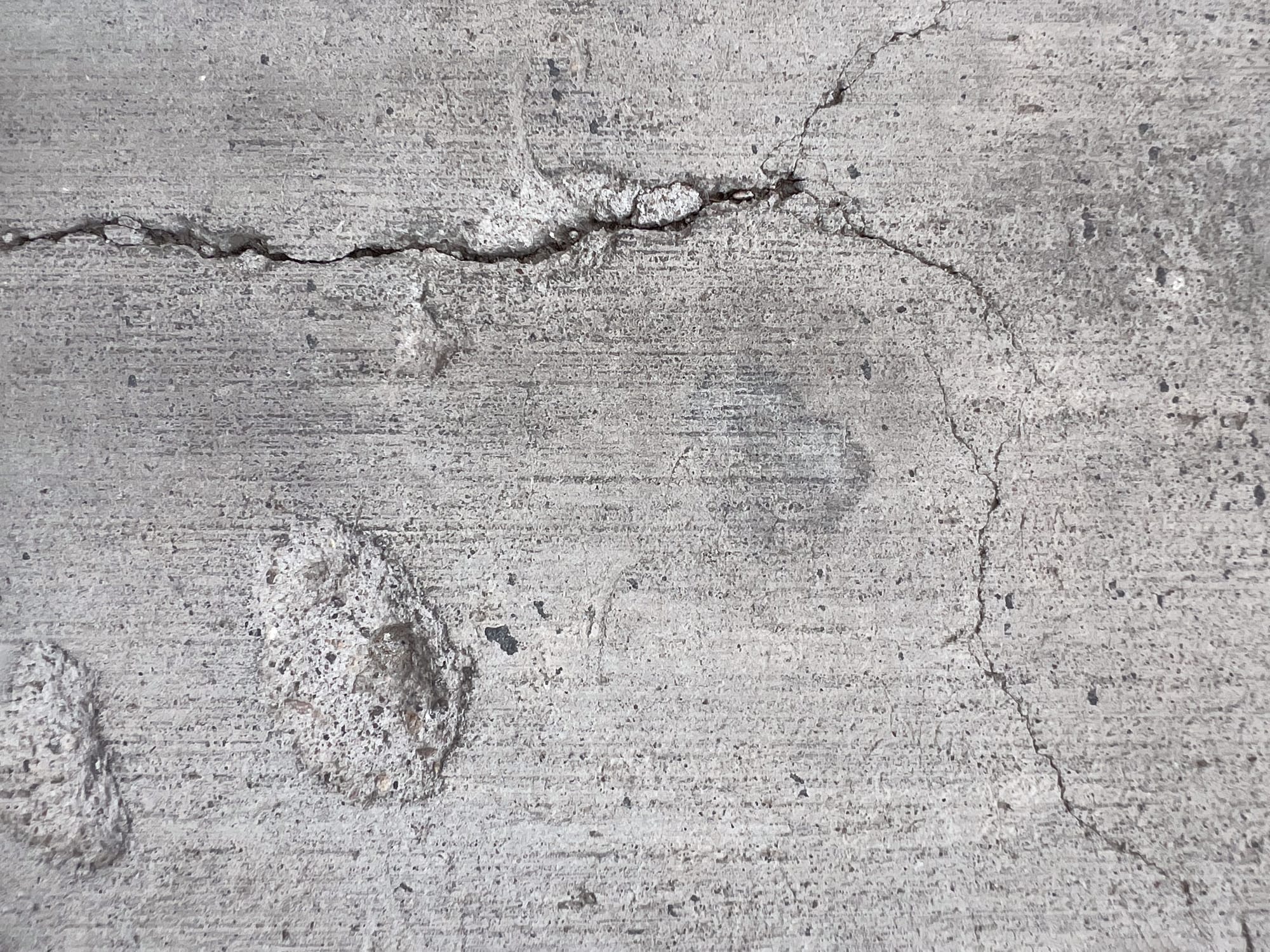 Close-up photograph of cracked concrete surface, showing fine lines and fractures that resemble scars or cuts, symbolising resilience and endurance.
