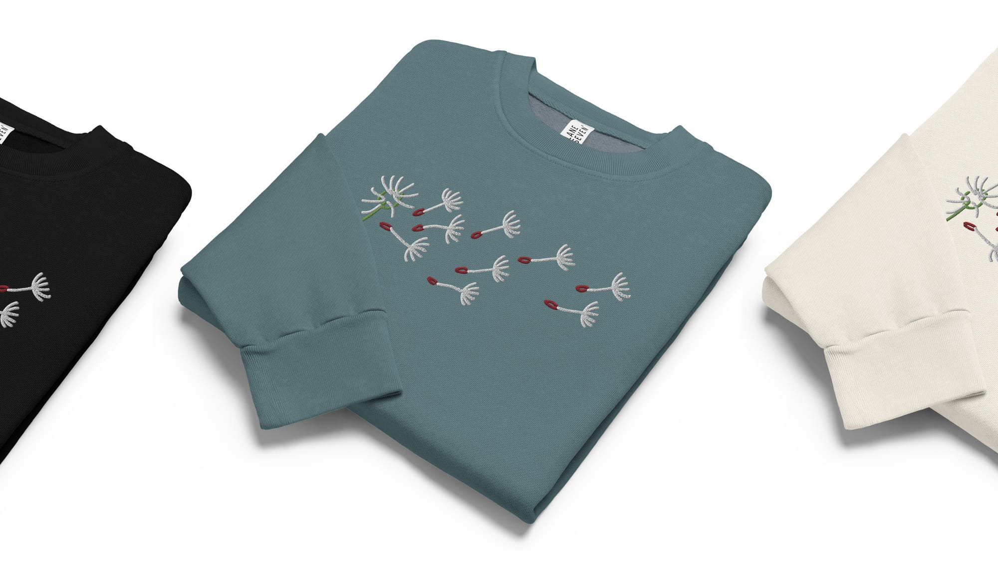 Folded crewneck sweaters featuring a clean embroidered dandelion with wind-blown seeds.